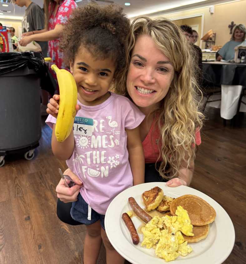 A widow mom with her daughter holding up a pancake breakfast with a banana 